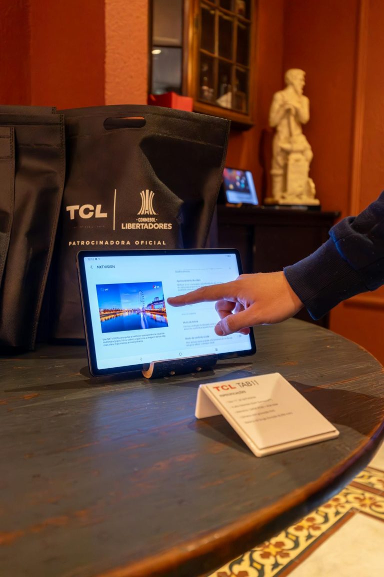 A hand interacts with a tablet display in a tech showroom featuring TCL products.